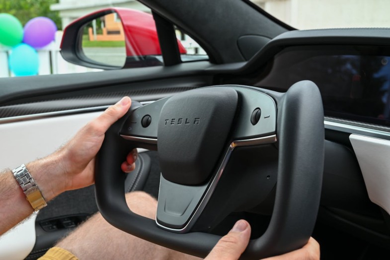 MAN HOLDING A YOKE SHAPED STEERING WHEEL OF A TESLA ELECTRIC CAR
