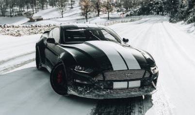A BLACK AND WHITE FORD SHELBY MUSTANG ON SNOW COVERED ROAD